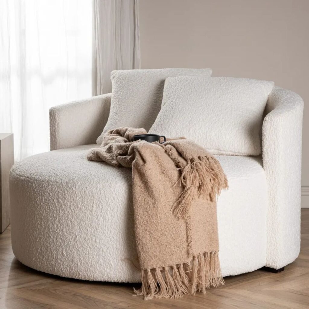 En beige rund soffa i teddy material som skapar en ljus och ombonad känsla i rummet En beige rund soffa i teddy material som skapar en ljus och ombonad känsla i rummet.